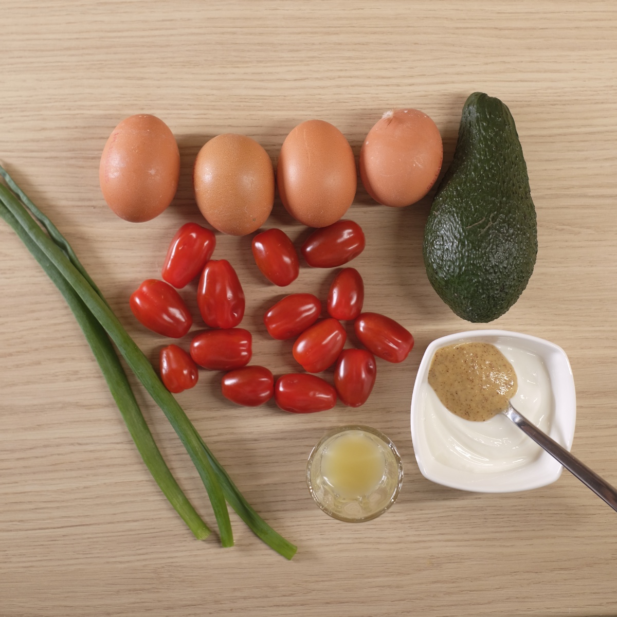 Avocado egg salad ingredients including eggs, avocado, cherry tomatoes, yogurt and chives on a wooden table