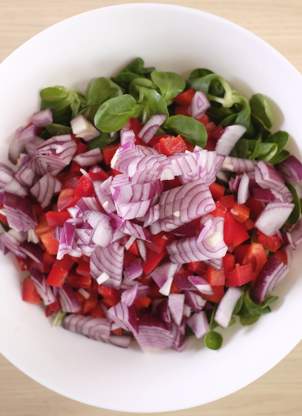 Lamb's lettuce, red pepper and red onion combined in a bowl for spicy egg salad