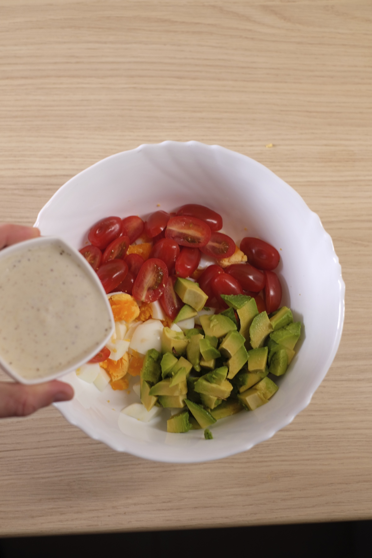 Adding creamy yogurt dressing to avocado egg salad ingredients in a bowl