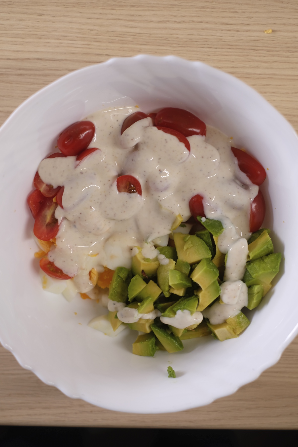 Avocado egg salad ingredients with dressing before mixing in a bowl