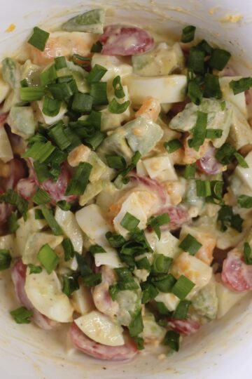 Creamy avocado egg salad with cherry tomatoes and chives ready to serve